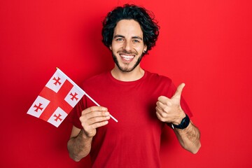 Poster - Handsome hispanic man holding georgia flag smiling happy and positive, thumb up doing excellent and approval sign