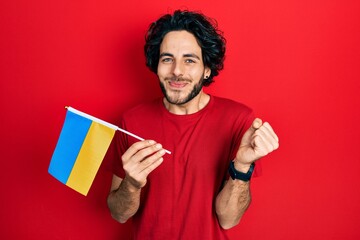 Sticker - Handsome hispanic man wearing ukraine flag screaming proud, celebrating victory and success very excited with raised arm