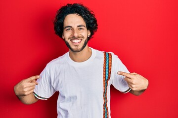 Sticker - Handsome hispanic man wearing casual white t shirt looking confident with smile on face, pointing oneself with fingers proud and happy.