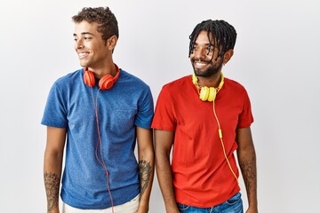 Wall Mural - Young hispanic brothers standing over isolated background wearing headphones looking away to side with smile on face, natural expression. laughing confident.