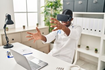 Sticker - Young african american man wearing doctor uniform using virtual reality glasses at clinic