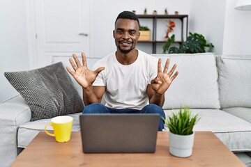 Wall Mural - Young african man using laptop at home showing and pointing up with fingers number nine while smiling confident and happy.