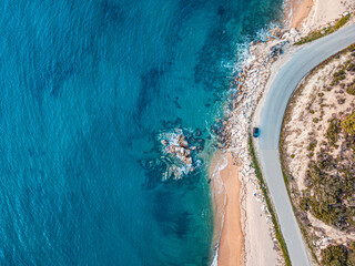 Wall Mural - Aerial view of an idyllic sea sandy beach with asphalt winding road and small car driving on. Background for travel and vacation