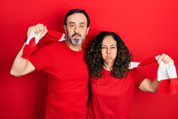 Poster - Middle age couple of hispanic woman and man wearing scarf team football hooligan cheering game puffing cheeks with funny face. mouth inflated with air, catching air.