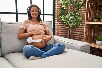 Wall Mural - Young latin woman pregnant listening to music put headphones on belly at home