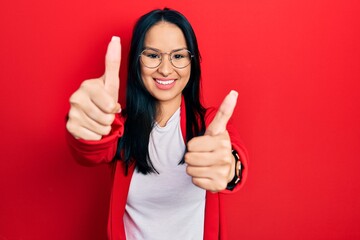 Beautiful hispanic woman with nose piercing wearing casual look and glasses approving doing positive gesture with hand, thumbs up smiling and happy for success. winner gesture.