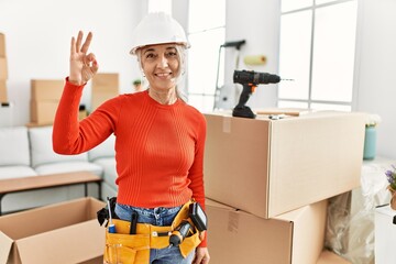 Canvas Print - Middle age grey-haired woman wearing hardhat standing at new home smiling positive doing ok sign with hand and fingers. successful expression.