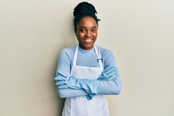 Poster - African american woman with braided hair wearing cleaner apron and gloves happy face smiling with crossed arms looking at the camera. positive person.