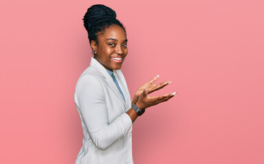 Canvas Print - Young african american woman wearing business clothes pointing aside with hands open palms showing copy space, presenting advertisement smiling excited happy