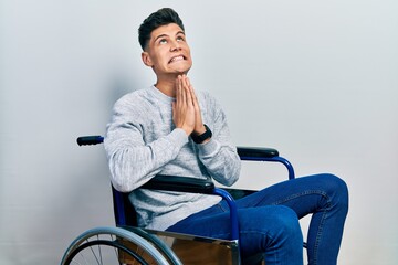 Canvas Print - Young hispanic man sitting on wheelchair begging and praying with hands together with hope expression on face very emotional and worried. begging.