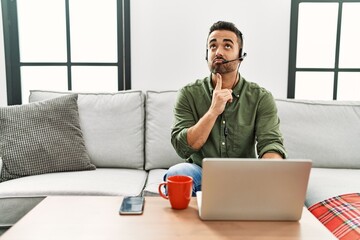 Poster - Young hispanic man with beard wearing call center agent headset working from home thinking concentrated about doubt with finger on chin and looking up wondering