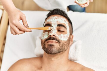 Canvas Print - Young hispanic man having facial mask treatment at beauty center