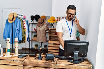 Sticker - Young hispanic man shopkeeper talking on the smartphone working at clothing store