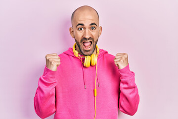 Canvas Print - Young bald man wearing gym clothes and using headphones celebrating surprised and amazed for success with arms raised and open eyes. winner concept.