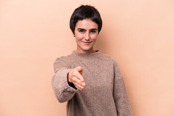 Young caucasian woman isolated on beige background stretching hand at camera in greeting gesture.