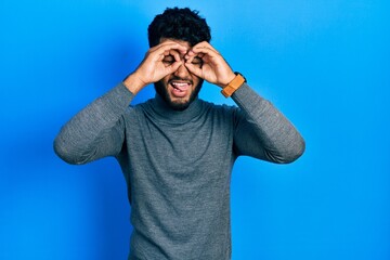 Sticker - Arab man with beard wearing turtleneck sweater doing ok gesture like binoculars sticking tongue out, eyes looking through fingers. crazy expression.