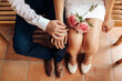Top view of Newlywed with their rings. Shoes of groom and bride and her small wedding bouquet of pink roses sitting and waiting in a wooden bench. Wedding day concept. Selective focus on the rings.