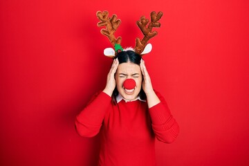 Poster - Young hispanic woman wearing deer christmas hat and red nose suffering from headache desperate and stressed because pain and migraine. hands on head.