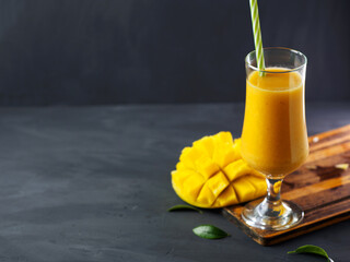 Wall Mural - Yellow exotic smoothie with mango in a glass with a straw. Dark background and copy space