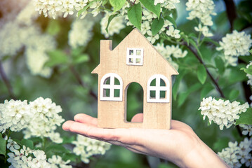 The girl holds the house symbol against the background of blossoming Bird cherry
