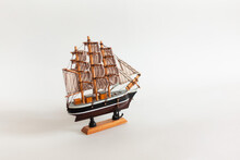 A Black Model Of Sail Ship With White Sails On A Wooden Rack. Isolated On The White Background