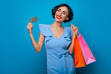 Young Smiling Gorgeous Brunette Woman With Shopping Bags And Credit Card In Hands Isolated On Blue Background