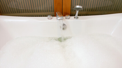 Sticker - Bathtub with soap suds. Preparing a bath, hot water flows from the tap. Foam with bubbles popping in warm water.