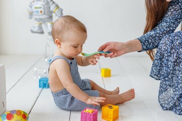 Mom feeds a one-year-old baby with a spoon while he plays with cubes