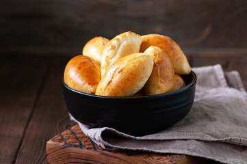 Potato stuffed hand pies - pirozhki in a black bowl on a wooden board with napkin.