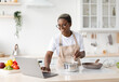 © Prostock-studio - Smiling millennial african american female in glasses, apron cooking, watching video lesson on laptop