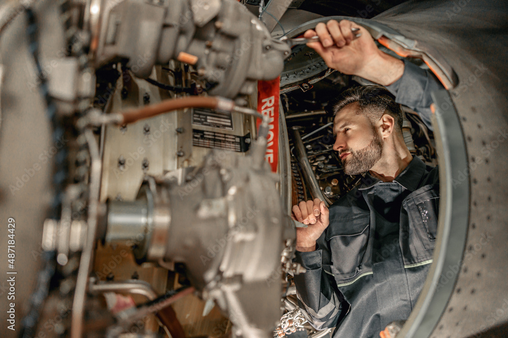 Male worker aviation maintenance technician using wrench while ...