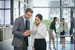 © Alexandra W/peopleimages.com - Keeping a close eye on the stock markets. Shot of a businessman showing something to his female colleague while they stand outside the boardroom.