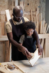 Wall Mural - Vertical portrait of caring African-American father teaching son in carpentry workshop