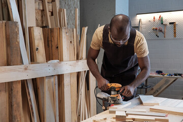 Wall Mural - Waist up portrait of mature black carpenter sanding wood using electric tool in workshop, copy space