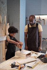 Wall Mural - Vertical portrait of cute African-American boy building wooden birdhouse while bonding with father in workshop