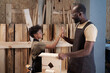 © pressmaster - Side view portrait of father and son high five while building wooden birdhouse in workshop together