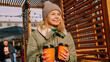 © brillianata - Woman carries two cups of mulled wine at the city outside food court. Street food festival, place to meet friends. She holds the cups forward.