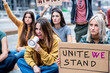 © MandriaPix - Young female protester giving a slogan using megaphone with group of people in background, women protesting for their empowerment and future