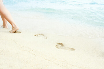 Wall Mural - A Beach travel - woman relaxing walking on a sandy beach leaving footprints in the sand. Close up detail of female feet on golden sand at a beach in Greece. Background.