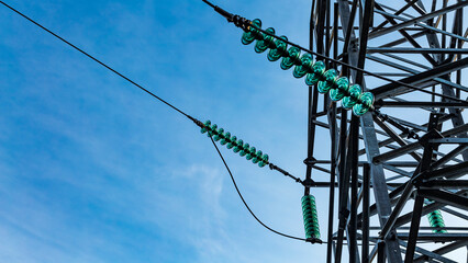 Close up of a transparent turquoise high voltage insulator or isolator in sunlight on electric tower on blue sky background. Electric power transmission line