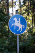 Ein Blau Weißes Schild mit einem Reitpferd markiert einen extra Reiterweg.
