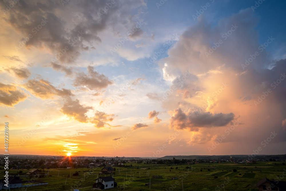 Dramatic sunset over rural area with stormy puffy clouds lit by orange ...