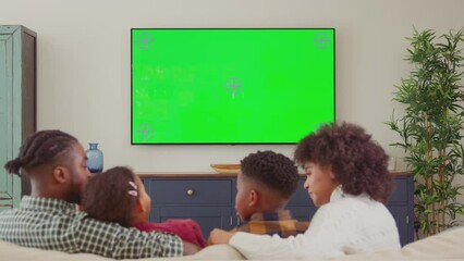 Wall Mural - Rear view of family sitting on sofa at home watching green screen TV and laughing at comedy - shot in slow motion