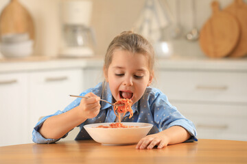 Wall Mural - Cute little girl eating tasty pasta at table in kitchen