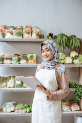 Wall Mural - Girl in veil selling vegetables smiling using a digital tablet