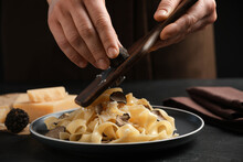 Woman slicing truffle onto tagliatelle at black table, closeup