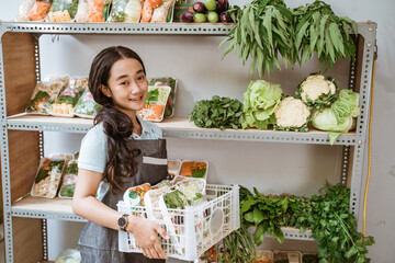 Wall Mural - Cute girl wearing apron carrying basket of fresh vegetables