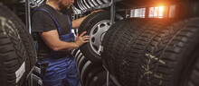 Tire At Repairing Service Garage Background. Technician Man Replacing Winter And Summer Tyre For Safety Road Trip.