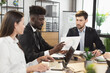 Multiracial business people in formal wear sitting at office desk with modern gadgets and having paperwork. Cooperation on common project. Business and finance concept.