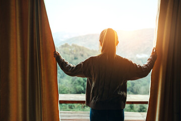 Woman opening curtains enjoy mountain view in morning, Happy traveller stay in hotel.